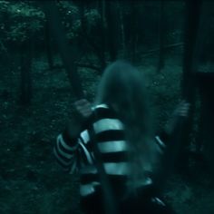 a woman with long hair is holding a bat in the woods at night, while wearing striped shirt and black pants