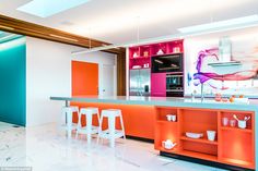 an orange and white kitchen with bar stools next to the counter top on marble flooring