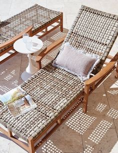 two chairs and a table on a patio with the sun shining through them, one chair has a pillow on it