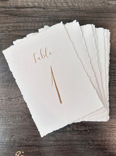 four folded cards with the word table on them and gold foiled numbers are placed next to each other