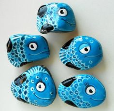 five blue fish shaped rocks with googly eyes on white surface, one is black and the other has four smaller ones