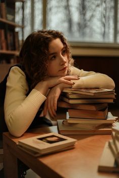 a woman sitting at a desk with stacks of books in front of her and looking off to the side