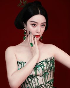 a woman in a green and white dress holding her hand to her face with palm leaves on it