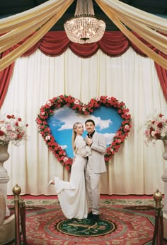 a man and woman standing in front of a heart shaped backdrop