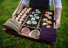 a person holding a tray full of sushi and sashimi on it's side