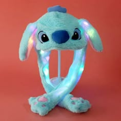 a blue stuffed animal with glowing lights on it's head and legs, sitting in front of a pink background