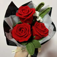 a hand holding a bouquet of red roses with green stems and white flowers in it