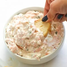 a hand dipping a piece of bread into a bowl of dip