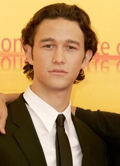 two young men are hugging each other in front of a yellow background and the man is wearing a black suit