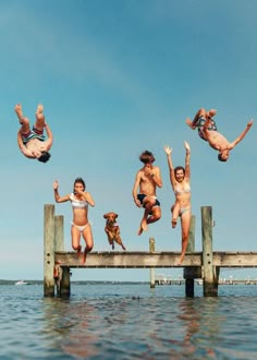 four people jumping off a dock into the water with their dog in front of them