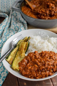 a white plate topped with rice and beans next to a bowl of chili, zucchini