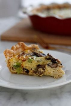 a slice of quiche on a white plate with a red casserole dish in the background