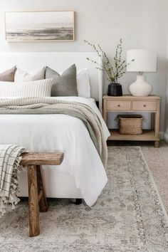 a white bed with pillows and blankets on top of it next to a wooden bench