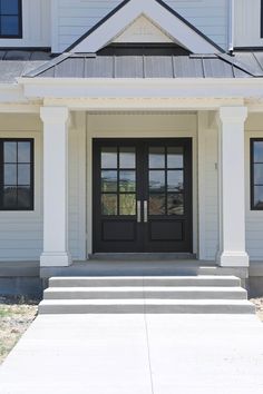 a white house with black doors and steps leading up to the front door that is open