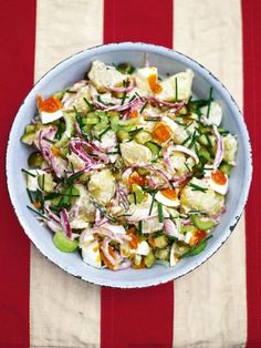 a blue bowl filled with salad on top of a red and white striped table cloth