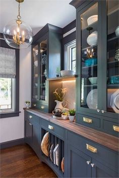 a kitchen with blue cabinets and white dishes on the counter top, along with hanging lights