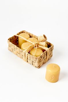 a wicker basket filled with yellow candles next to a candle holder on a white surface