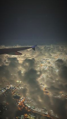 an airplane wing flying above the clouds in the night sky with city lights below it