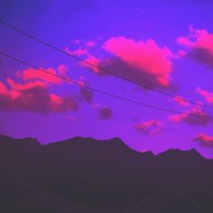 the sky is purple with pink clouds and power lines in front of some mountains at sunset