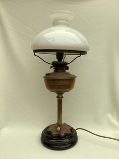 an old fashioned lamp with a white shade on it's base and a cord plugged in