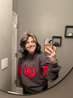 a woman taking a selfie in front of a mirror with her cat sweatshirt on