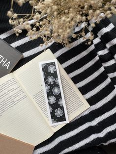 an open book on top of a black and white striped blanket next to some flowers