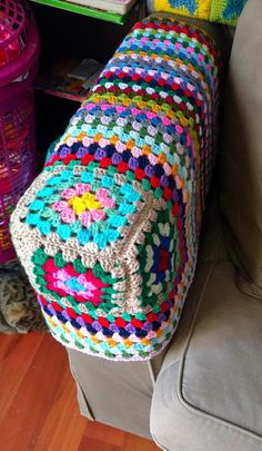 a crocheted granny blanket sitting on top of a couch next to a book shelf