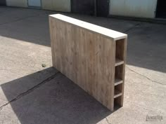 a wooden shelf sitting on top of a cement floor next to two garage doors and an empty parking lot