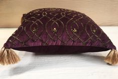 a purple pillow with tassels on it sitting on a white tablecloth next to a wooden wall