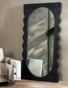 a large mirror sitting on the side of a wall next to a white chair and window