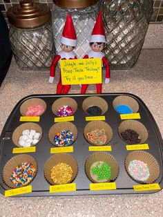 an elf is sitting next to some cupcakes on a tray with candy and marshmallows