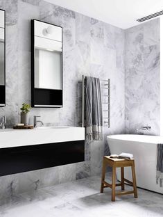 a white bath tub sitting next to a bathroom sink under two mirrors and a wooden stool