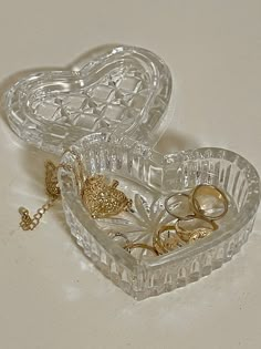 two clear heart shaped boxes filled with wedding rings and gold jewelry on a white surface