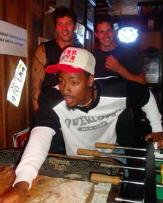 three men are standing behind a table with food on it and one man is wearing a hat