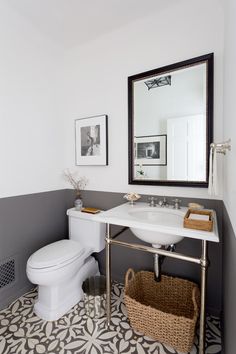 a white toilet sitting next to a sink in a bathroom under a mirror and framed pictures on the wall