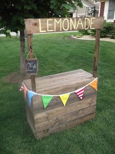 a wooden lemonade stand in the grass with bunting and flags hanging from it