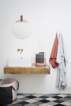 a white sink sitting next to a mirror on top of a wooden shelf in a bathroom