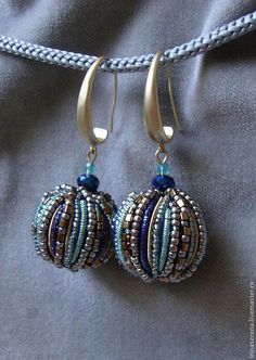 two blue and gold beaded earrings hanging from a string on top of a gray cloth