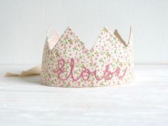 a pink and green floral crown with the word love on it's side, sitting on a white surface