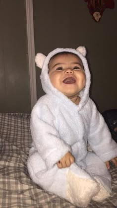 a baby in a bear costume sitting on a bed with his mouth open and tongue out