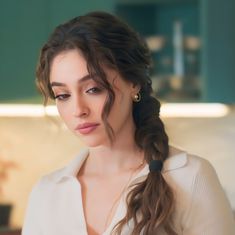 a woman with long hair wearing a white shirt and gold hoop earrings looking at the camera