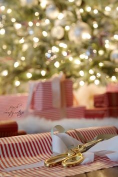 a pair of scissors sitting on top of a wrapped present box in front of a christmas tree