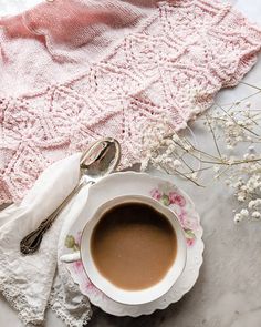 a cup of coffee sits on a saucer next to a pink blanket and flowers