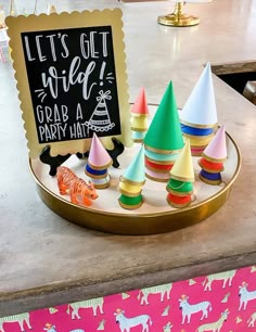 colorful party hats sitting on top of a gold tray next to a sign that says let's get wild grab a party hat