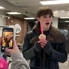 a man holding up a cell phone to take a picture of another person eating an ice cream cone