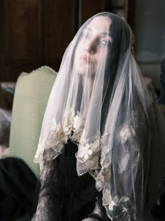 a woman wearing a veil with flowers on it's head is sitting in a chair