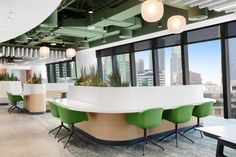 an office with green and white chairs, desks and plants in the windowed area