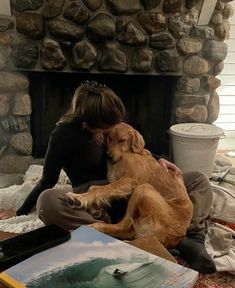 a woman sitting on the floor with her dog in front of a stone fire place