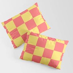 two pink and yellow checkered pillows sitting on top of each other in front of a white background