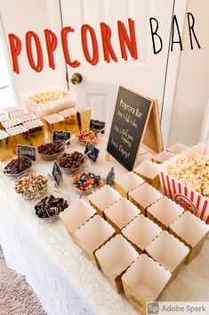 a table topped with lots of different types of foods and desserts next to a sign that says popcorn bar